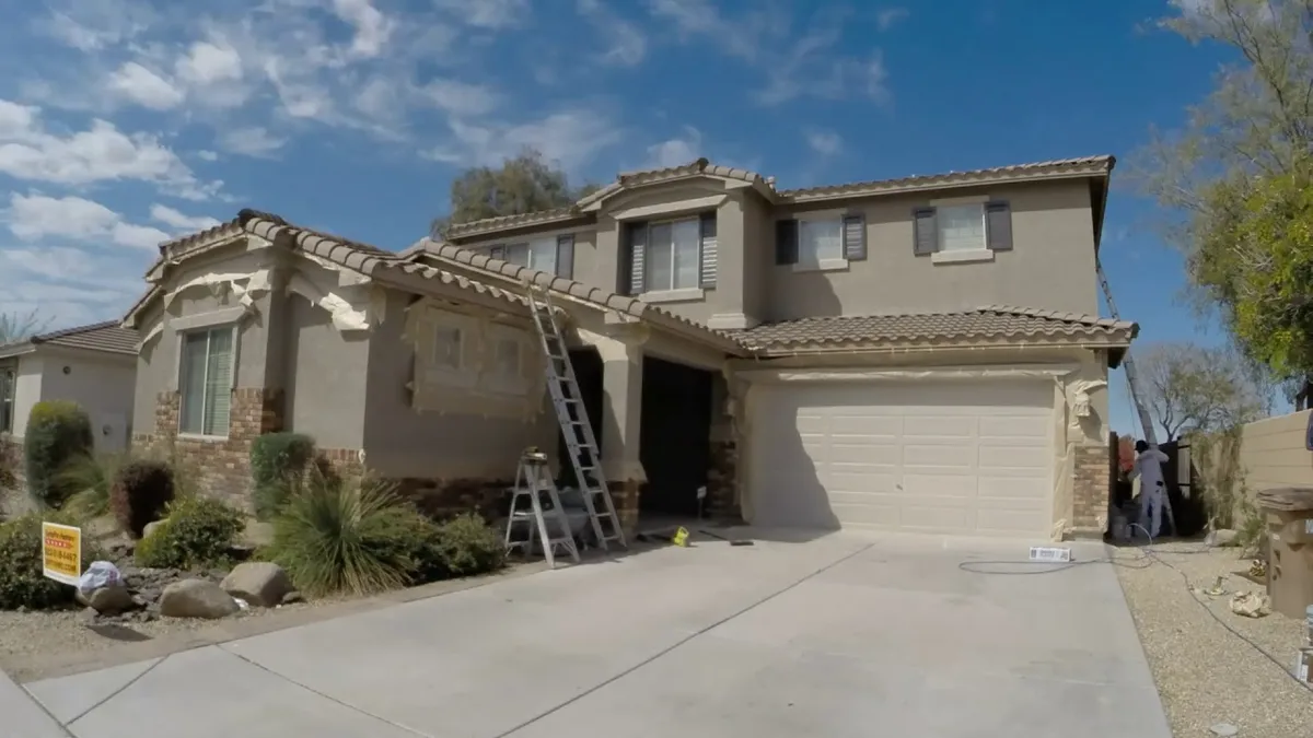 Exterior house painting in progress showing ladder setup and stucco preparation on residential home